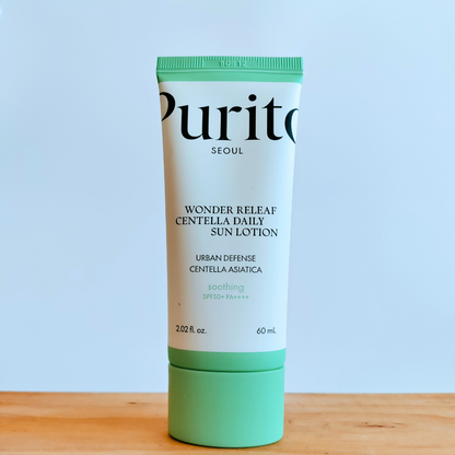 Tube of Purito Wonder Releaf Centella Daily Sun Lotion on a wooden surface with a light blue background