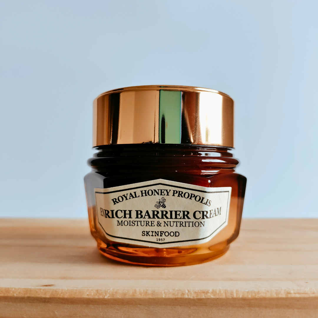 Skinfood Rich Barrier Cream jar with gold lid on a wooden surface and light blue background